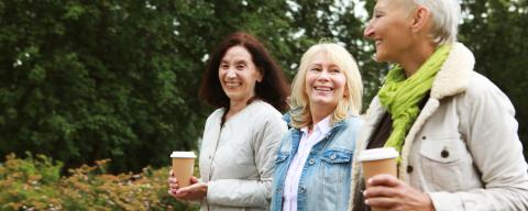Charming elderly women friends are walking, talking and drinking coffee. 